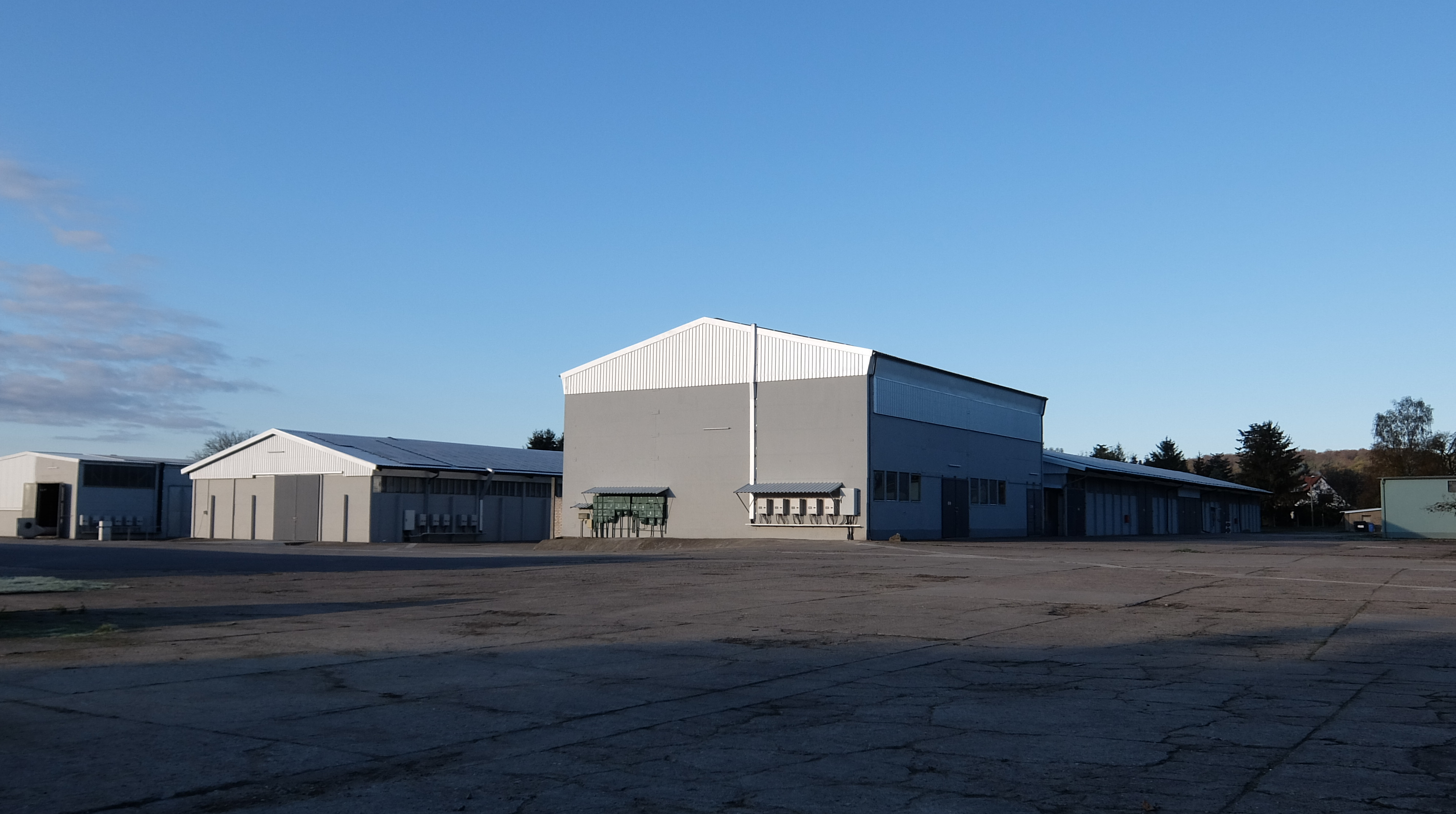 Große graue Industriehalle mit Nebengebäuden und breiter Asphaltfläche.