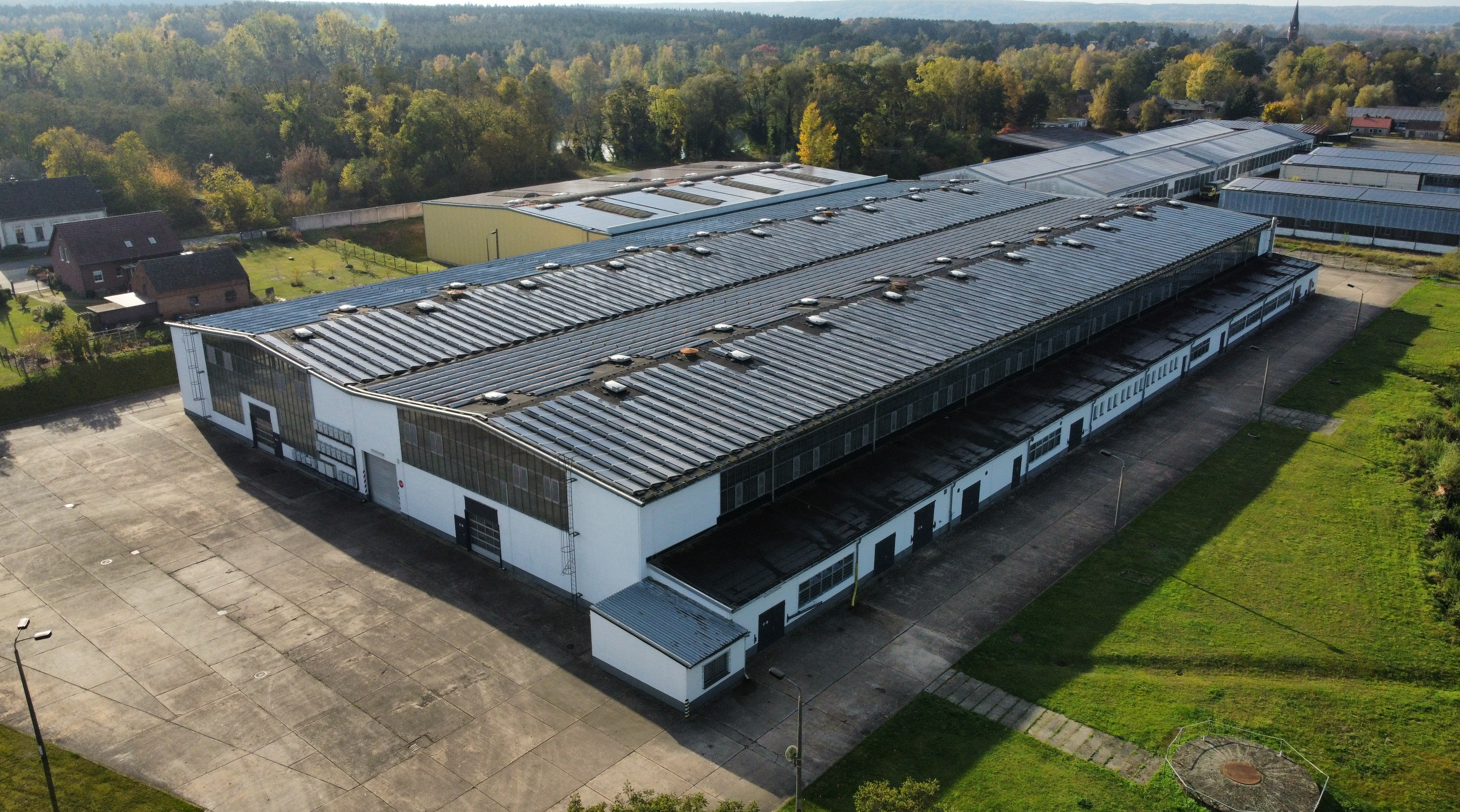 Große Industriehalle mit langem Dach und umliegender Grünfläche.