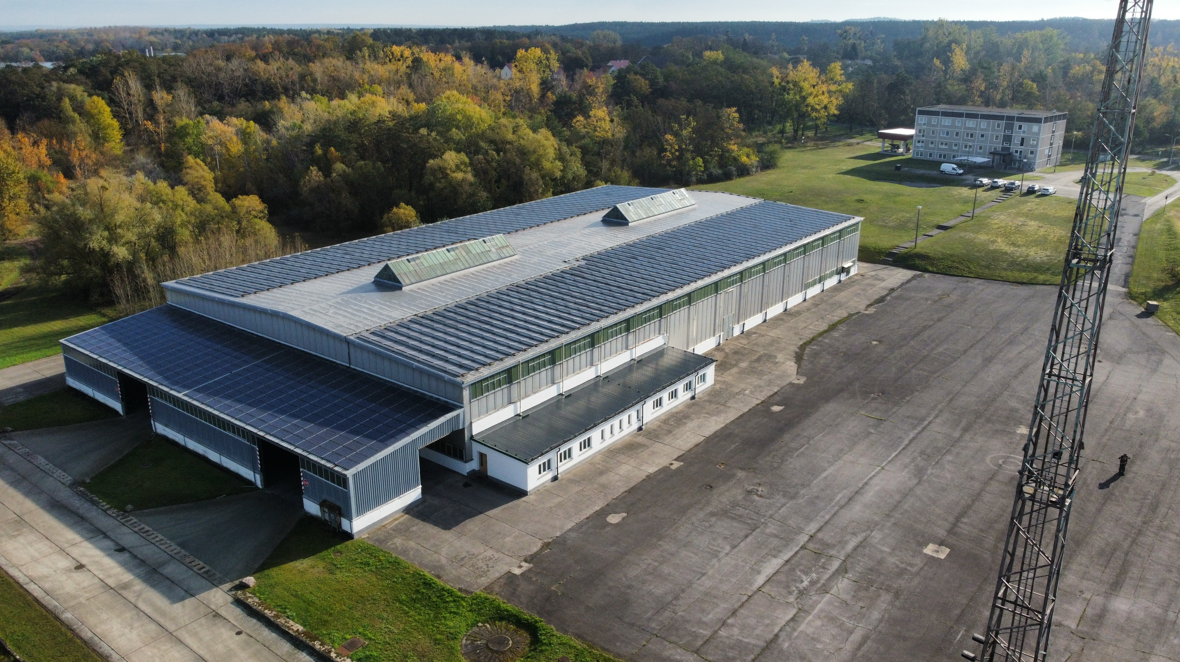 Große Halle mit Glasfront, Asphaltfläche und umliegender Grünbereich.