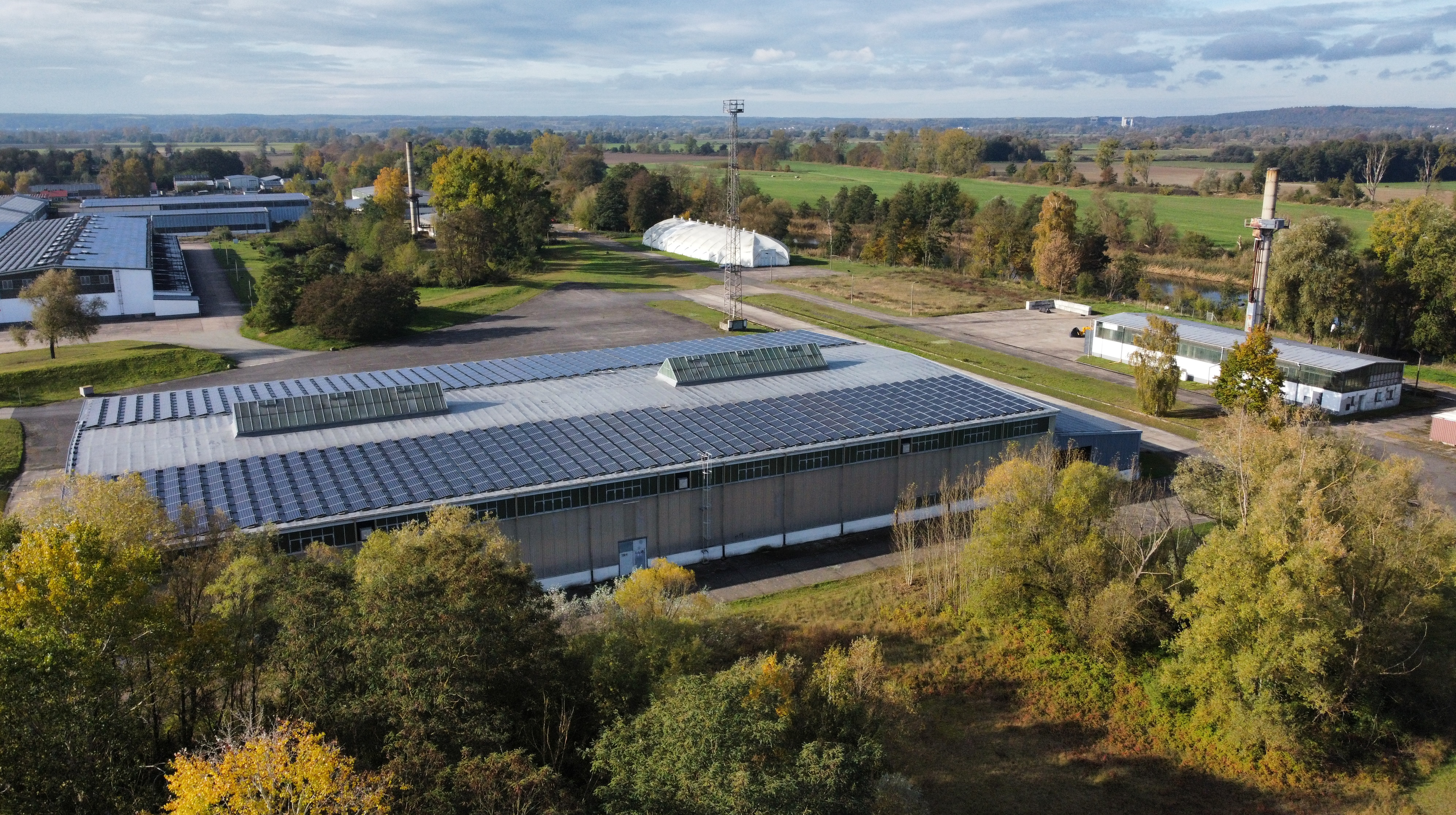 Industriehalle mit Solardach, umgeben von Bäumen und Grünflächen.