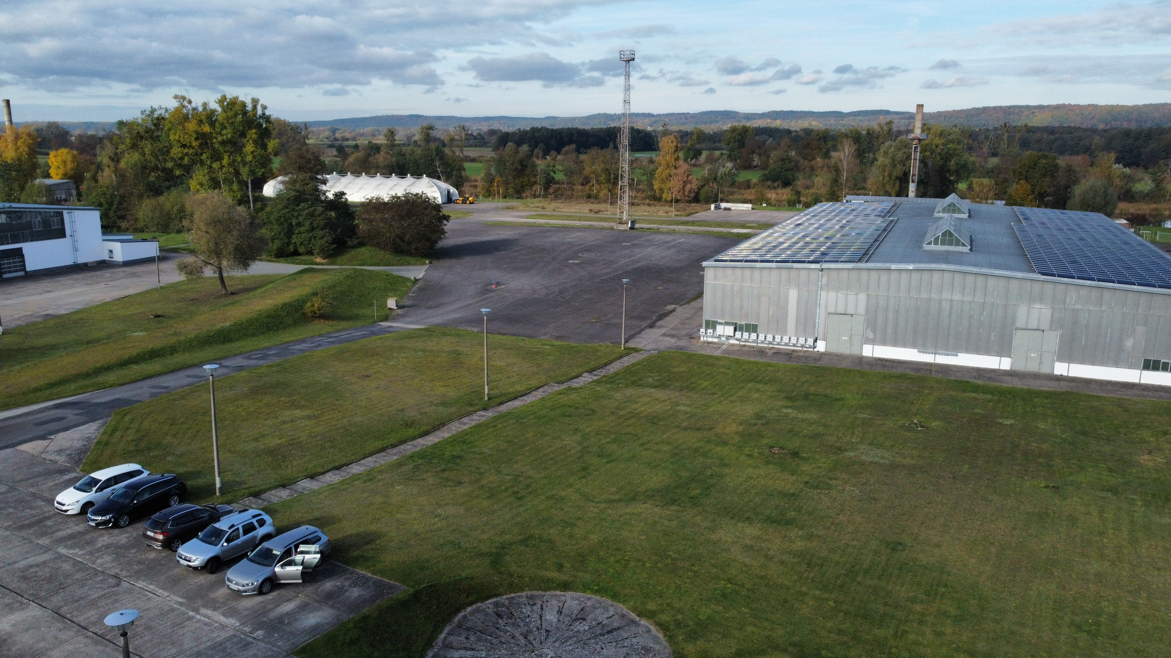 Industriehalle mit Solardach, davor Grünfläche und geparkte Autos.