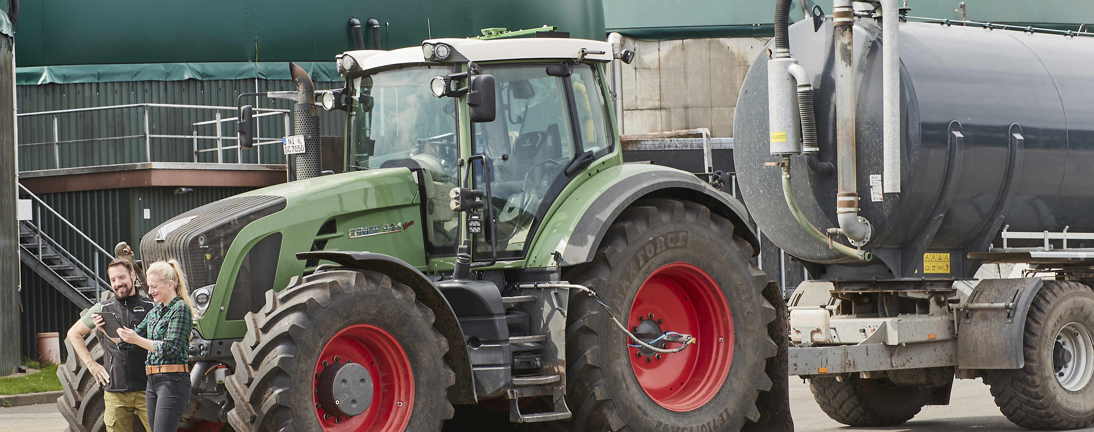 Zwei Personen, im Hintergrund ein Traktor mit Güllefass und eine Biogasanlage.