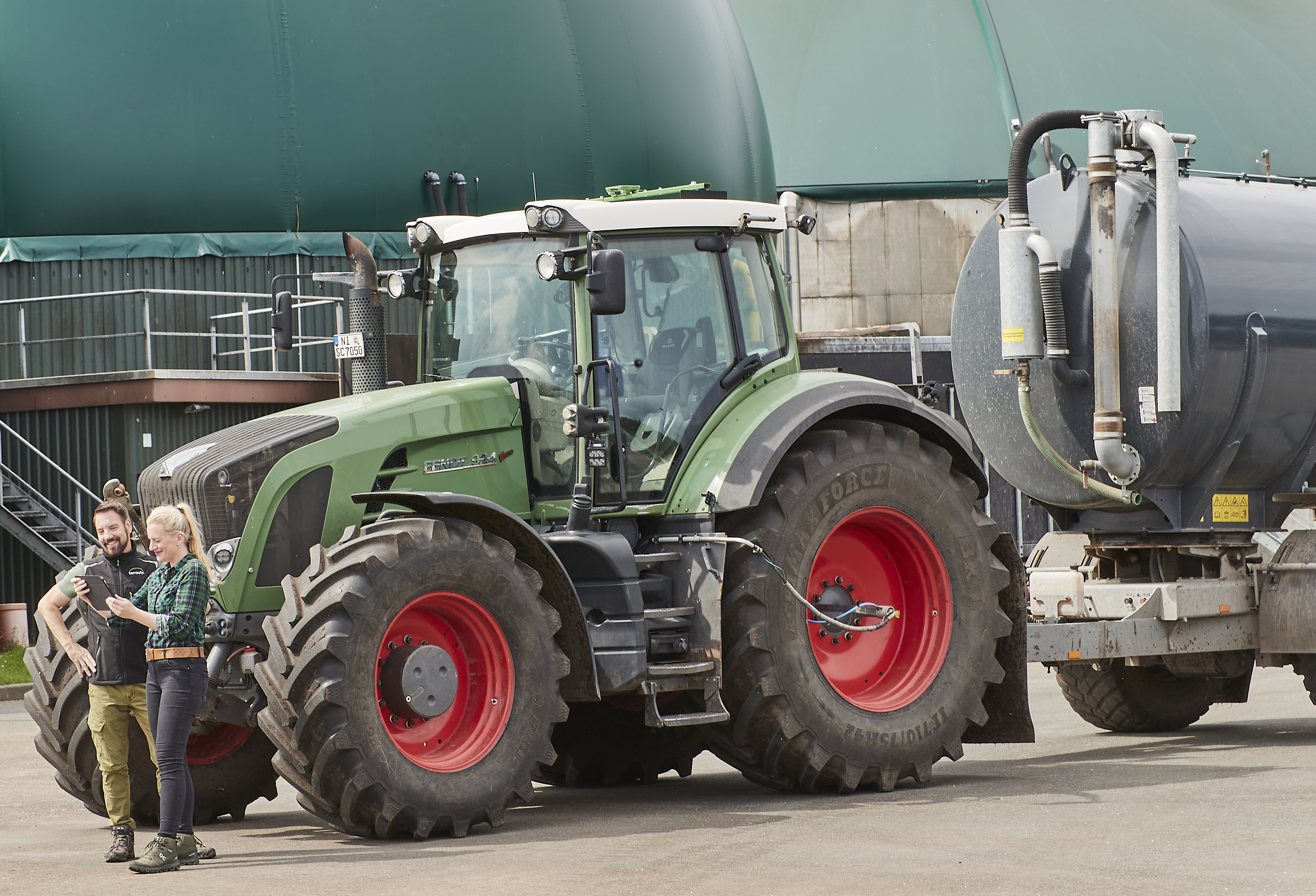 Zwei Personen, im Hintergrund ein Traktor mit Güllefass und eine Biogasanlage.