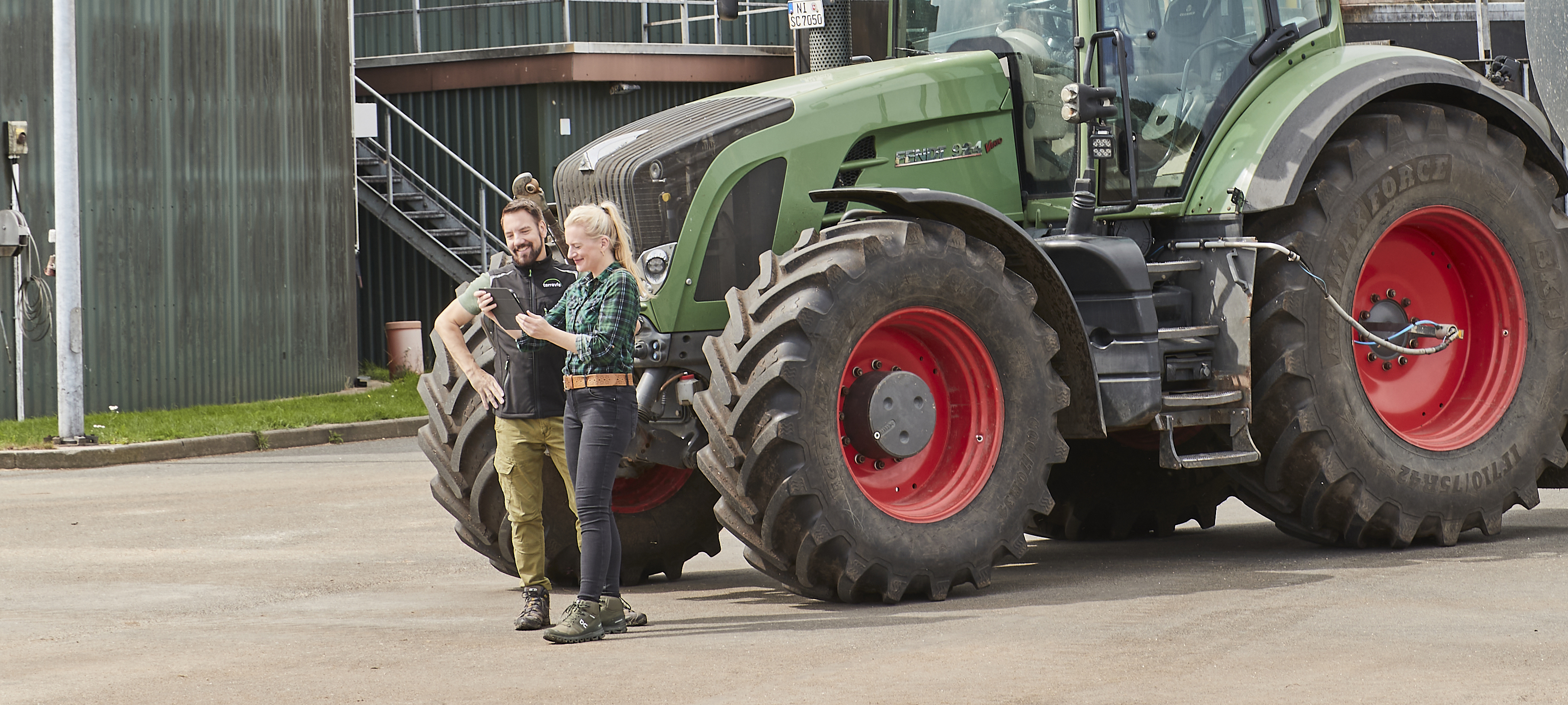 Zwei Personen, im Hintergrund ein Traktor mit Güllefass und eine Biogasanlage.