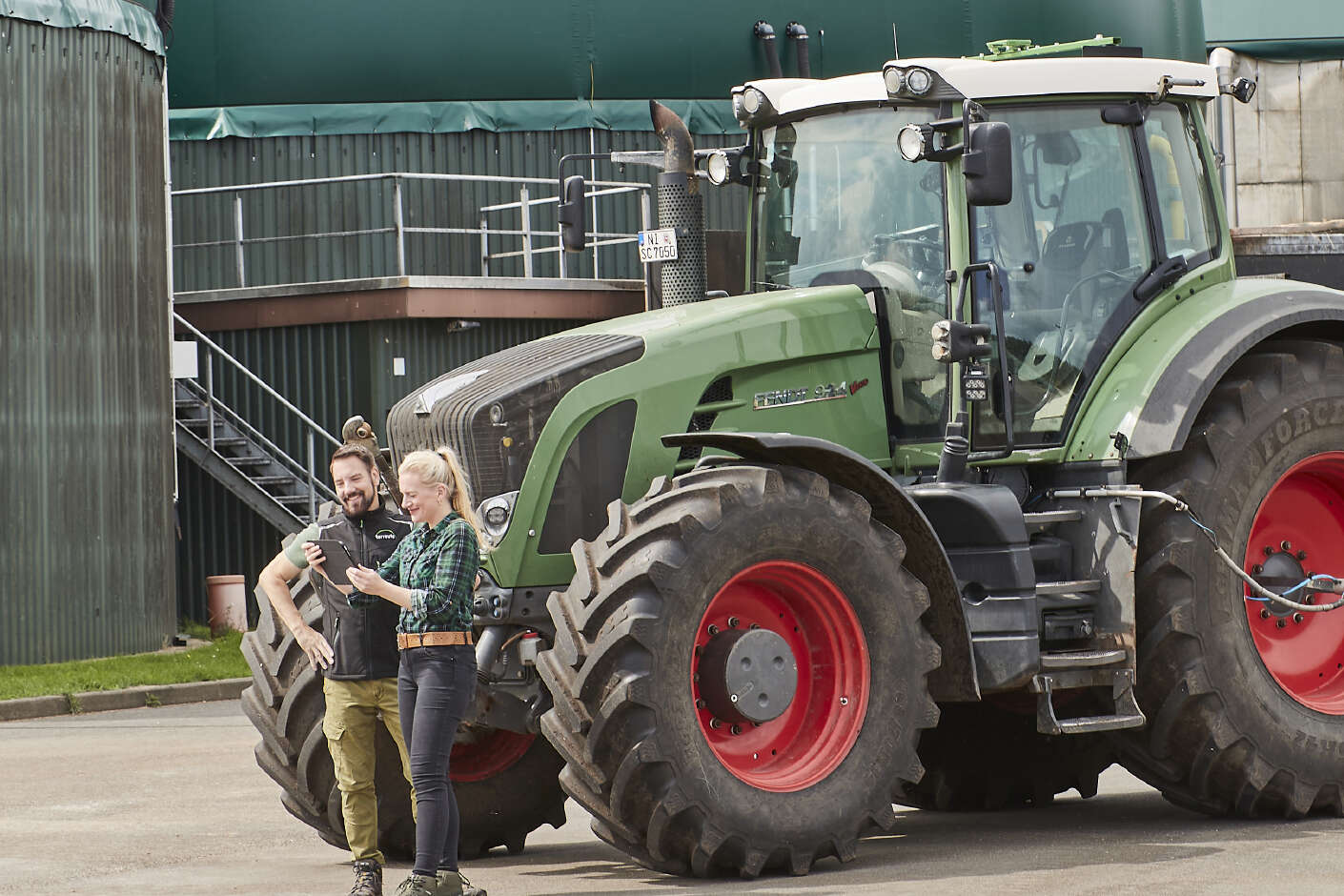 Zwei Personen, im Hintergrund ein Traktor mit Güllefass und eine Biogasanlage.