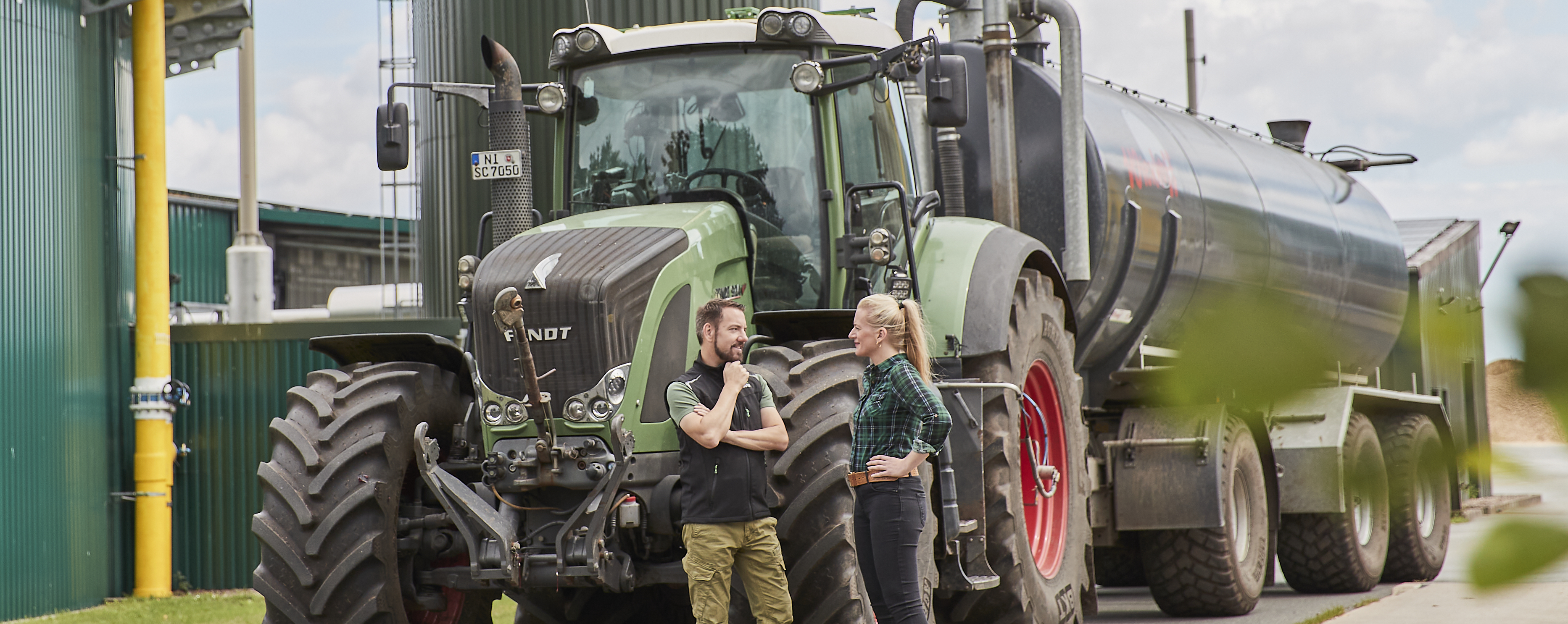 Eine landwirtschaftliche Biogasanlage, ein Trecker fährt im Vordergrund.