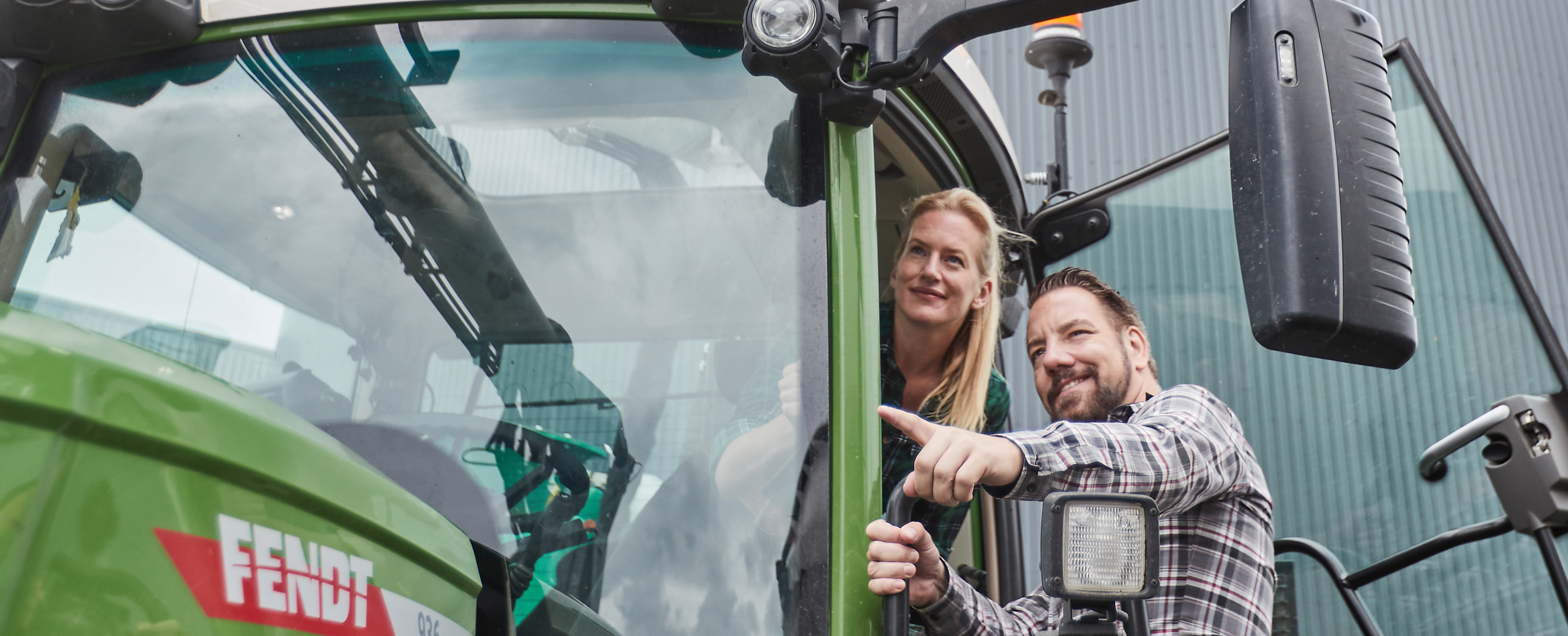 Zwei Personen auf einem Traktor vor einer Biogasanlage.