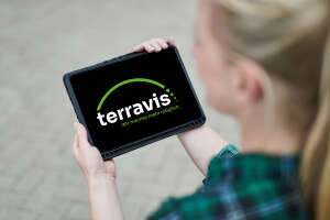 Eine Frau hält ein Tablet. Auf dem Tablet sind das Terravis Logo. 