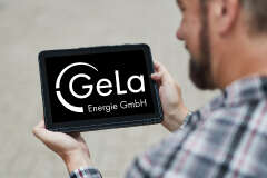Ein Mann hält ein Tablet. Auf dem Tablet sind das Gela Logo. 