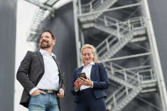 Zwei Personen im Bsuiness-Look vor einer Biogasanlage