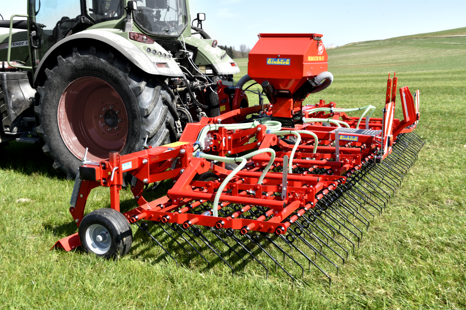 Ein Schlepper mit einem Striegel fährt über Grünland