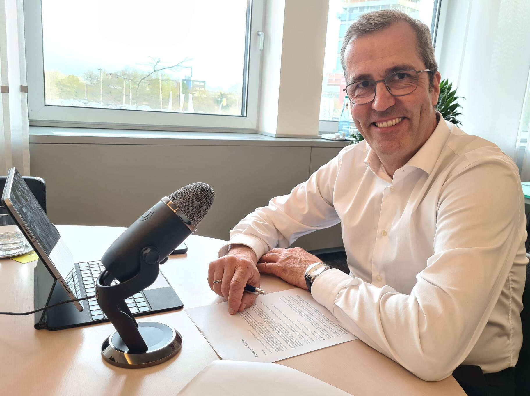 Dr. Dirk Köckler sitz in seinem Büro vor Tablet und Podcast-Mikrofon. 