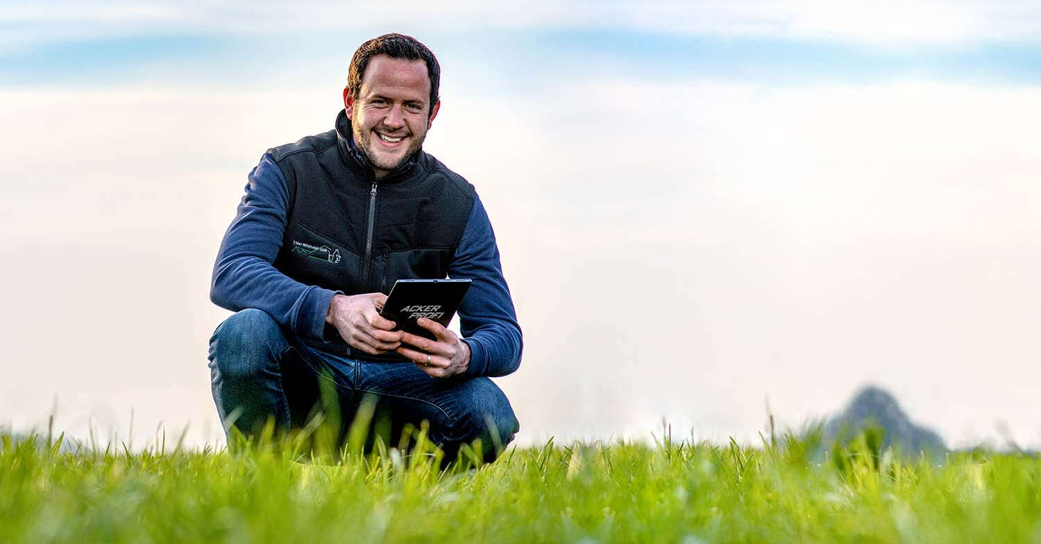 Mann hockt mit Tablet auf Feld