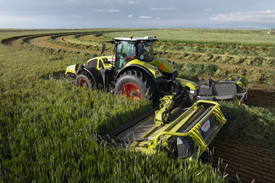 CLAAS Traktor mit Großflächenmähwerk bei der Ernte von Grünfutter auf weitläufigem Feld aus der Voge