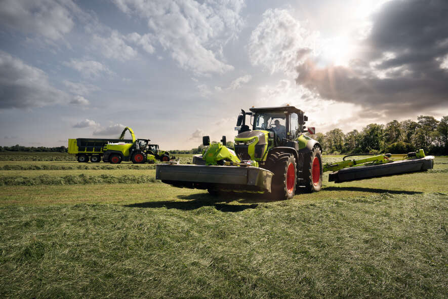CLAAS Traktor mit Großflächenmähwerk bei der Grünlandernte im Abendlicht auf weitläufiger Wiese.