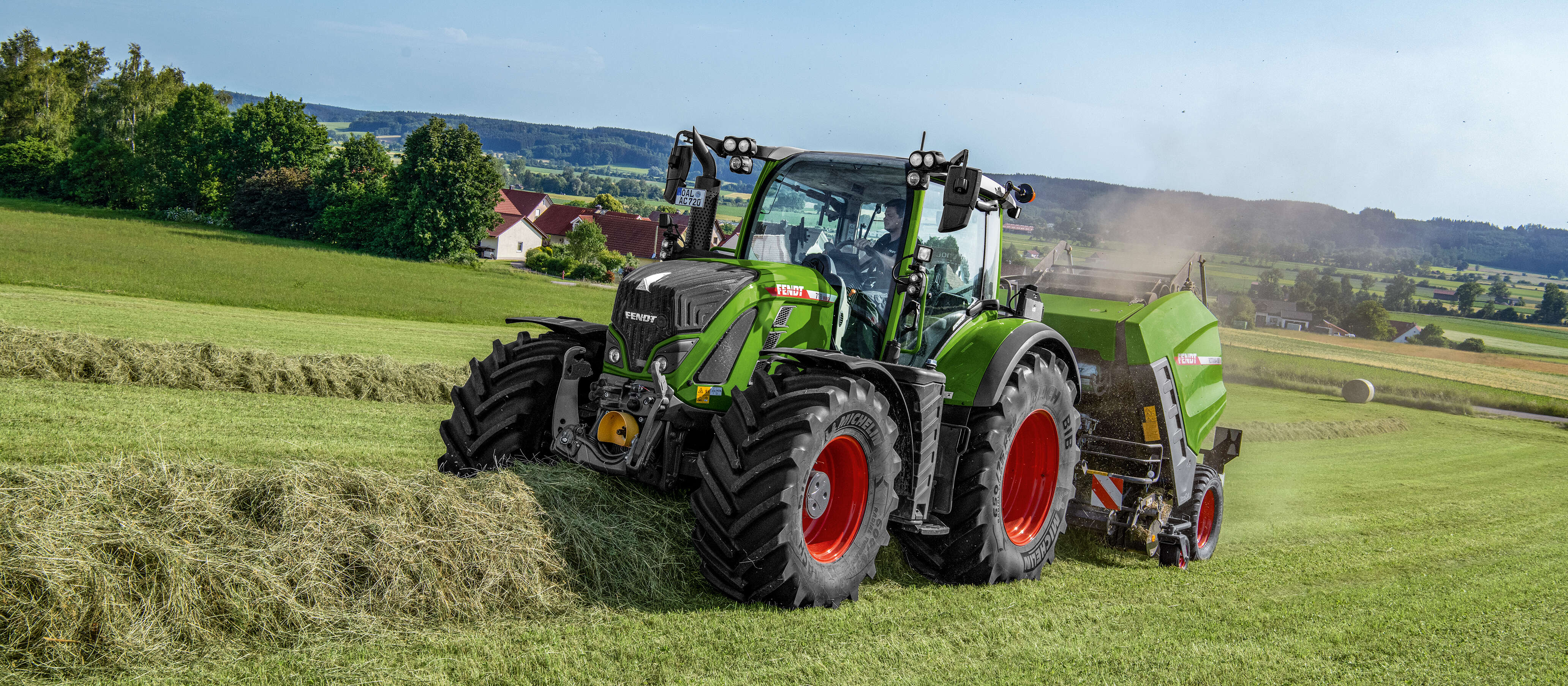 Fendt 700 Vario mit Rundballenpresse beim Pressen von Heu auf hügeliger Grünlandfläche.