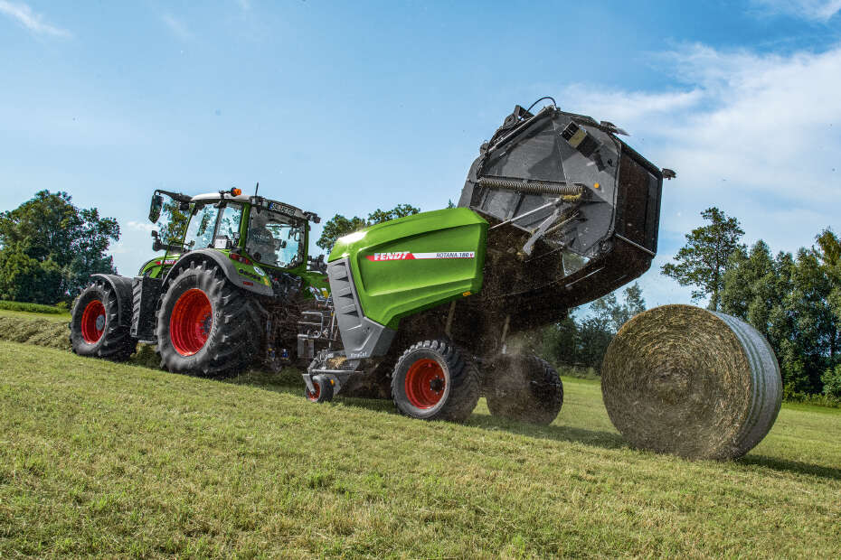 Fendt 700 Vario mit Rundballenpresse beim Auswerfen eines gepressten Heuballens auf dem Feld.