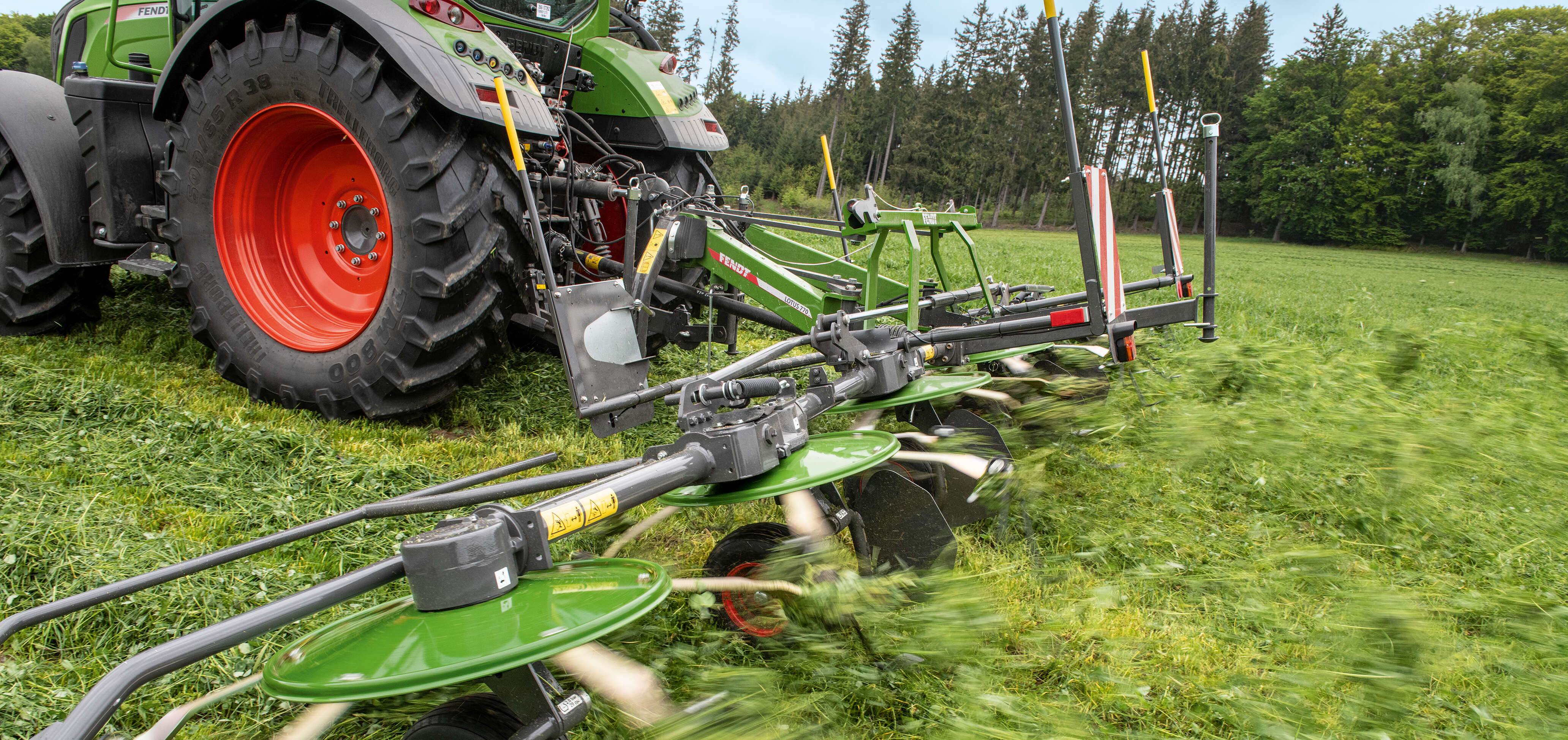 Fendt 300 Vario mit Kreiselzettwender beim Verteilen von Grünfutter auf einer Wiese.