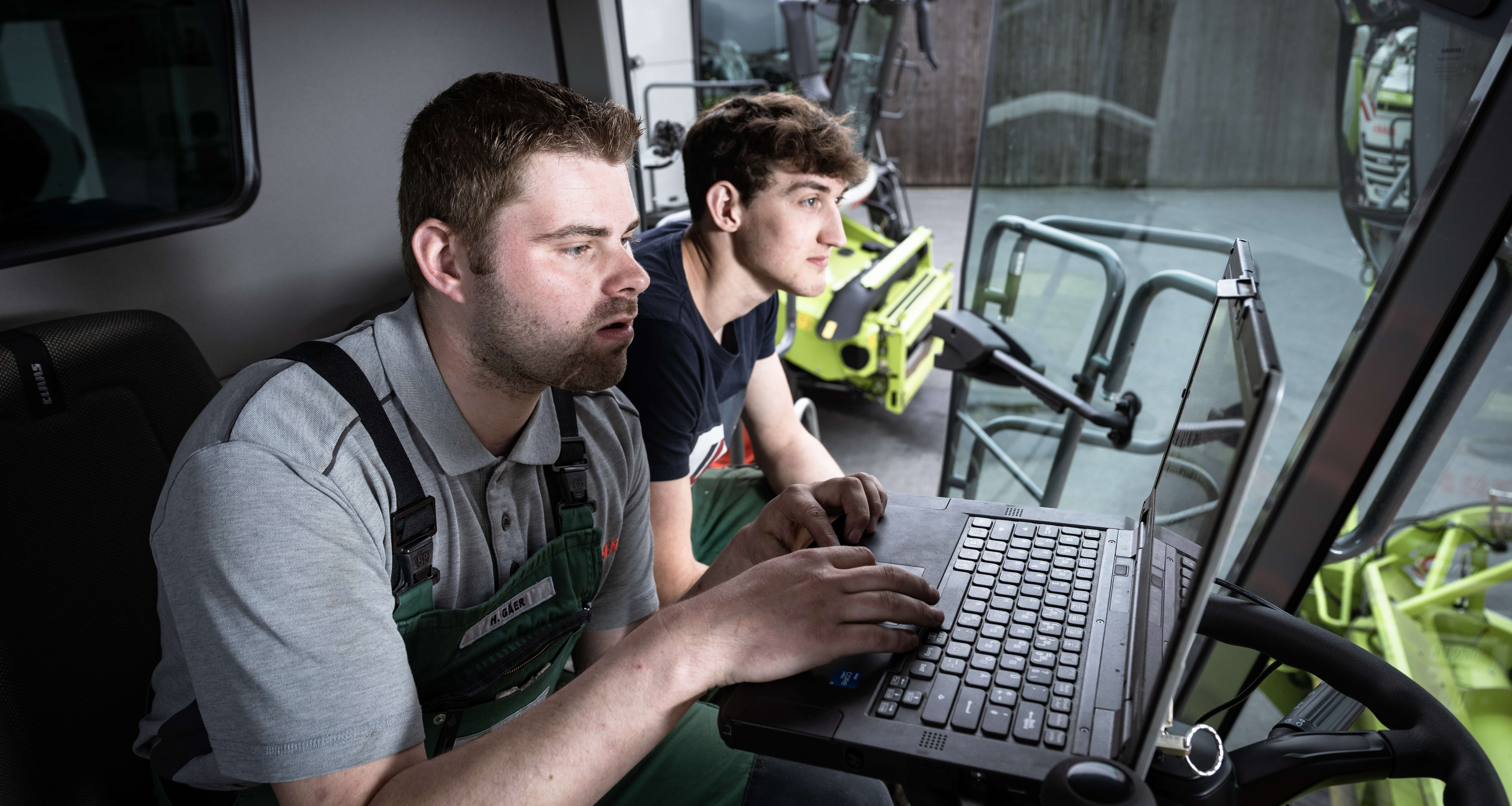 Mitarbeiter analysieren Maschinendaten am Laptop in der Kabine eines CLAAS Feldhäckslers.