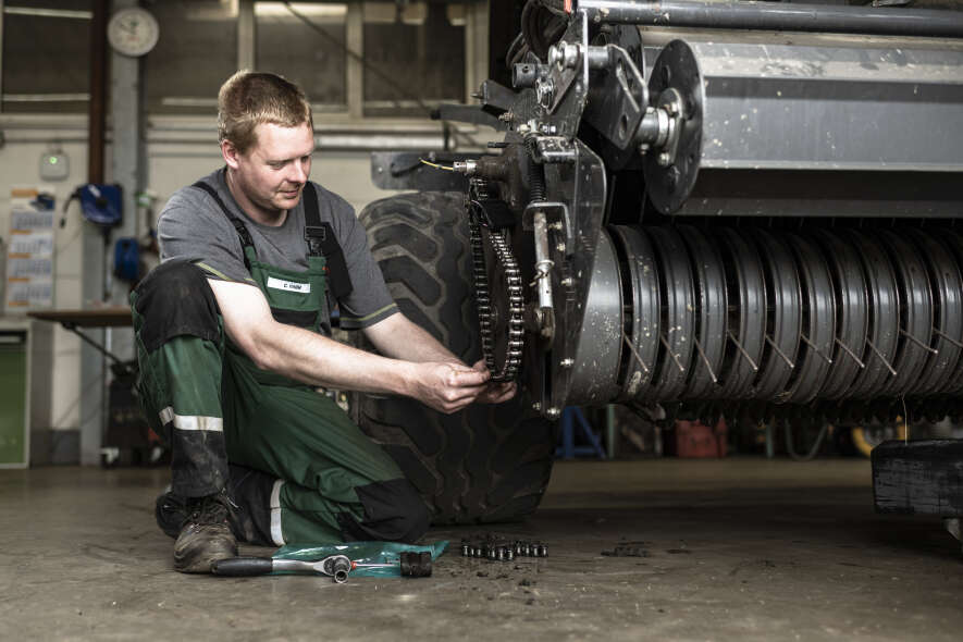 Werkstattmitarbeiter wartet Antriebskette an landwirtschaftlicher Ballenpresse in der Werkstatt
