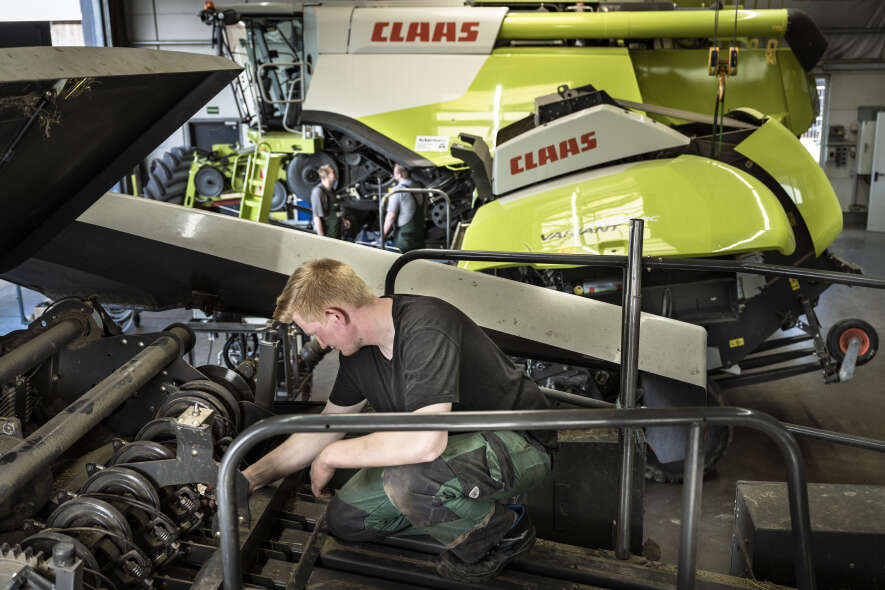 CLAAS Mähdrescher in der Werkstatt, Mitarbeiter führt Wartungsarbeiten an der Erntetechnik durch