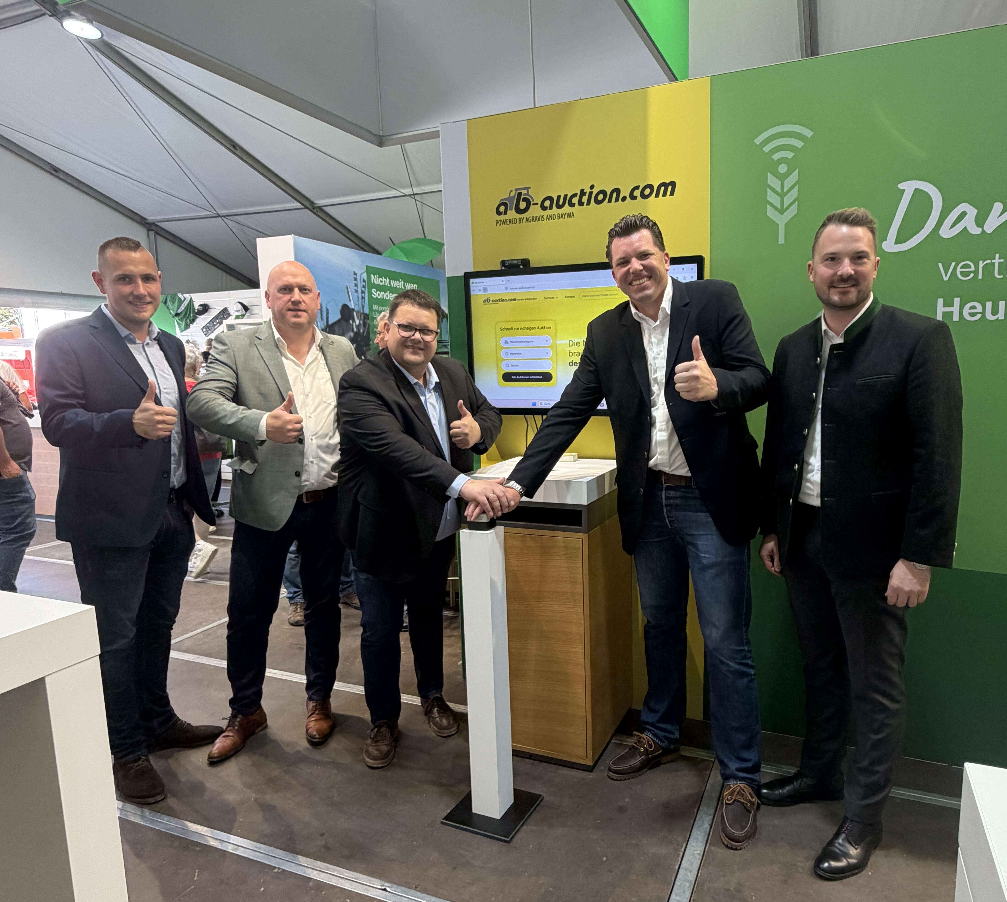 Fünf Männer drücken einen Buzzer vor einem Schild mit dem Logo von ab.auction