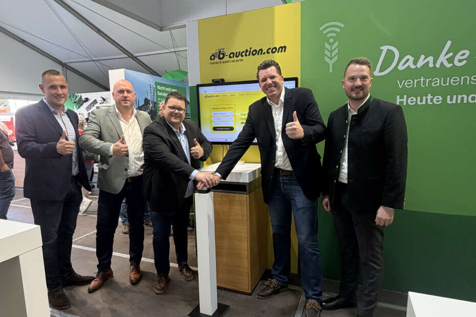 Fünf Männer drücken einen Buzzer vor einem Schild mit dem Logo von ab.auction
