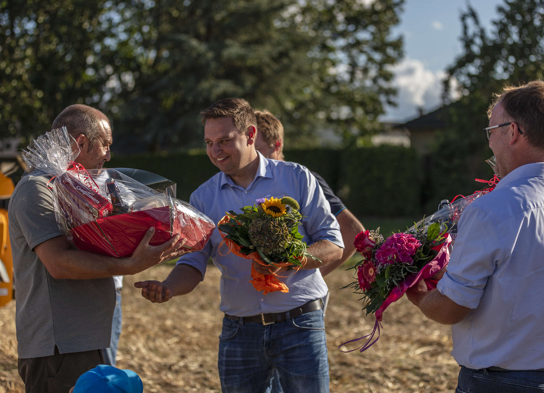 Übergabe von Blumen und Präsentkörben auf einer Feldveranstaltung.