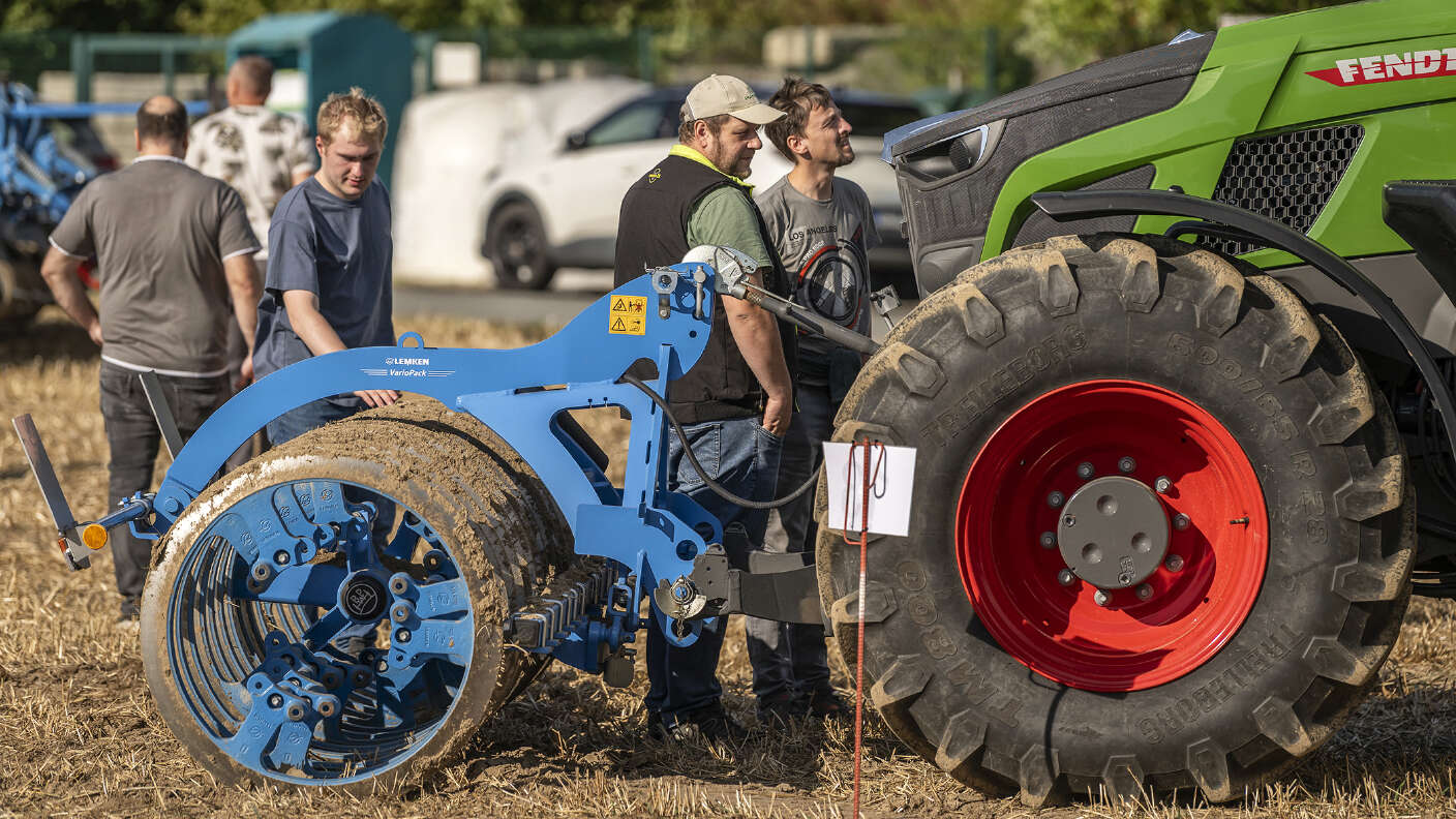 Fendt Traktor mit Bodenbearbeitungsgerät und Besuchern auf einem Stoppelfeld.
