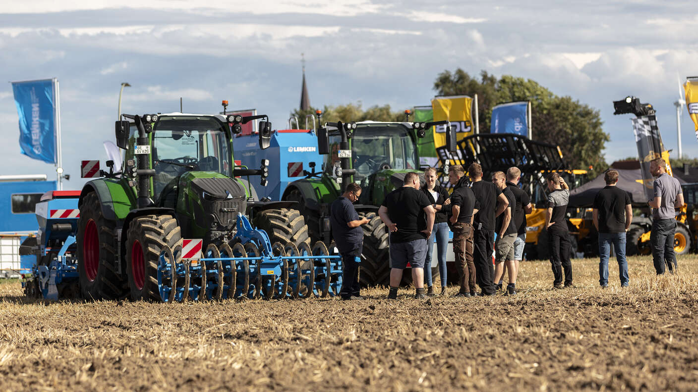 Fendt Traktoren mit Bodenbearbeitungsgeräten und Besuchern auf einem Ackerfeld.