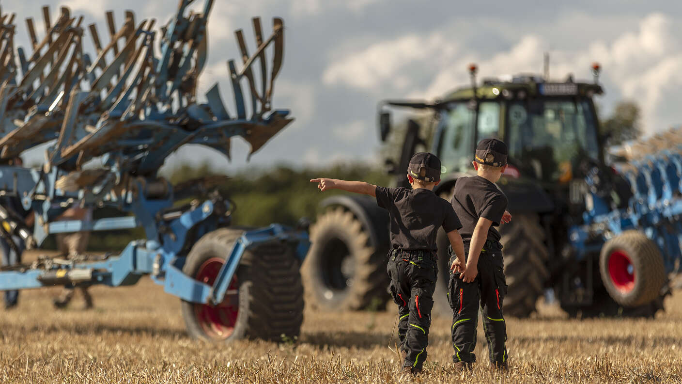 Kinder vor Landtechnik auf einem Stoppelfeld bei einer Feldvorführung.