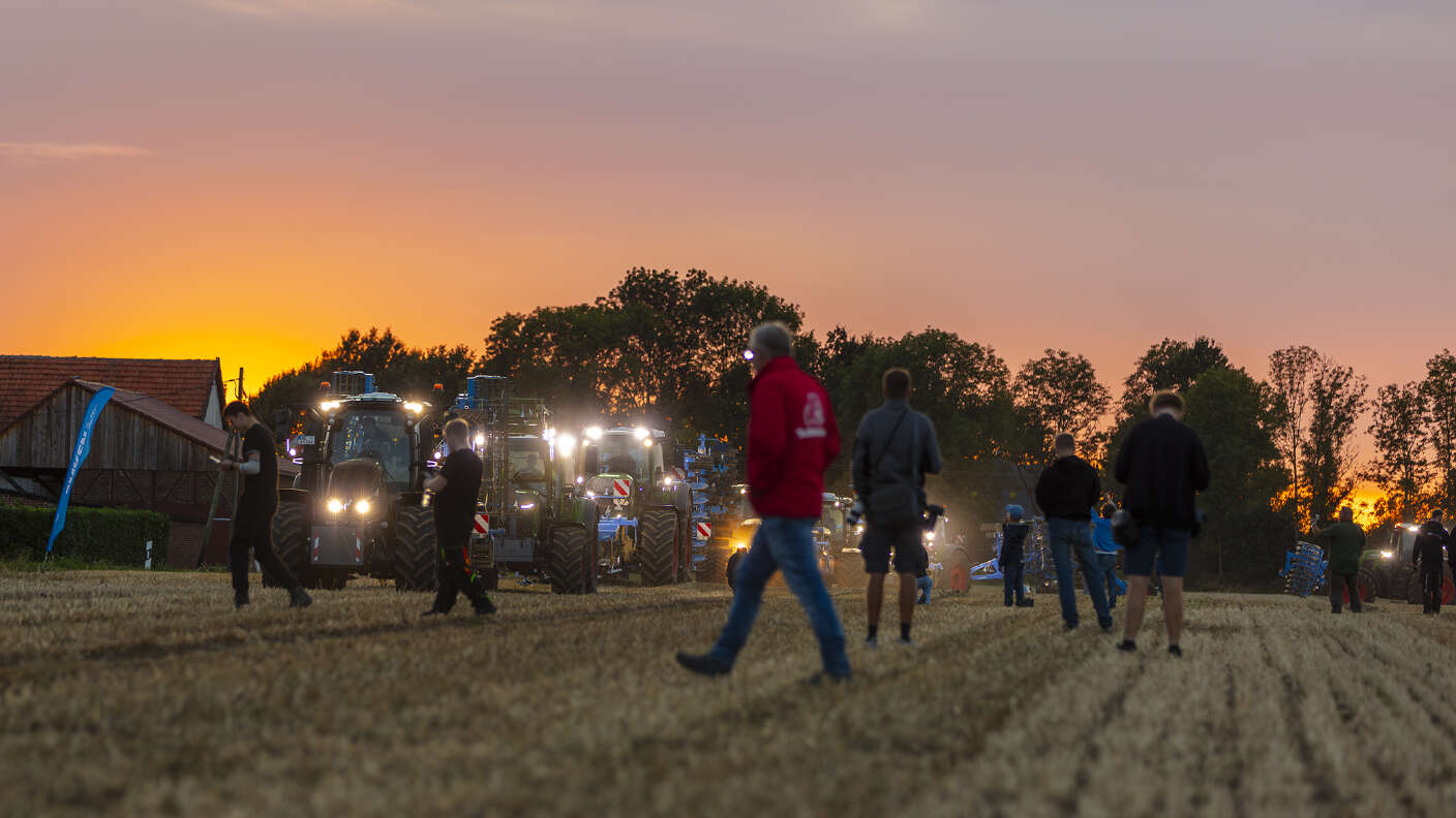 Fendt Traktoren und Besucher auf einem Stoppelfeld bei Sonnenuntergang.