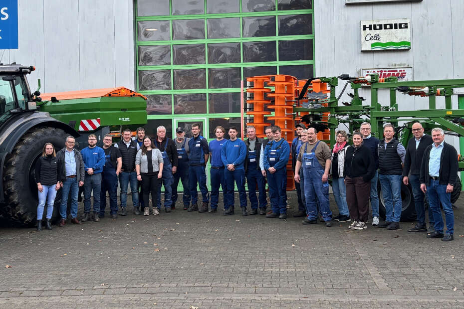 Eine Gruppe von Menschen steht vor Landmaschinen und einer Halle mit dem Schild VR PLus Technik.